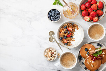 breakfast top view, pancakes, croissants, granola with yogurt, berries, nuts and coffee on a white marble background, copy space
