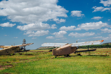 Abandoned, destroyed, rusty old planes stand on the grass under a blue sky with white clouds.