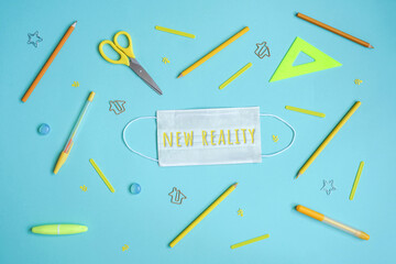 Stationery on blue. Bright stylish flat lay. Different yellow tools with protective mask in centre. New reality lettering.