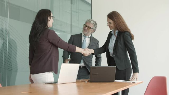 Positive friendly business colleagues closing deal, standing up and shaking hands with each other at end of meeting. Medium shot. Handshake concept