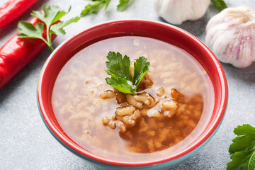 Vegetarian soup kharcho with rice and vegetables. Garlic hot pepper tomatoes. Grey concrete table, Ceramic dishes.