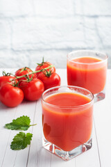 Tomato juice in glass glasses and fresh ripe tomatoes on a branch. White wooden background with copy space.