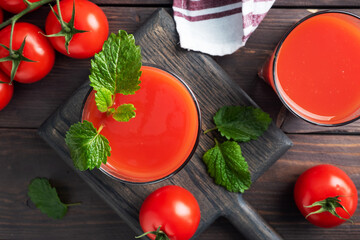 Tomato juice in glass glasses and fresh ripe tomatoes on a branch. Dark wooden background with copy space.