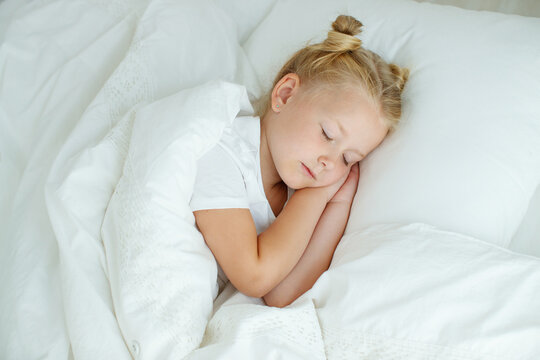 Little girl in bed with white linen. A child at home in the morning wakes up in his room. High quality photo.