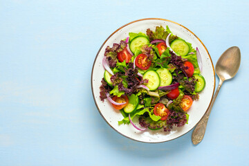 Healthy vegetable salad of cherry tomatoes, cucumber slices, green and purple lettuce leaves, onions and olive oil in plate on blue table Top view Flat lay Diet, mediterranean menu Vegan food