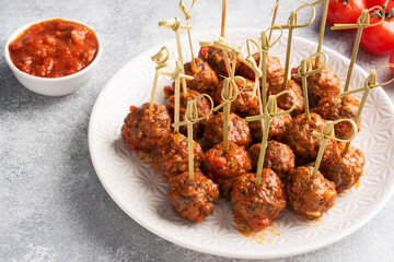 Beef meatballs stewed in tomato sauce on a plate on barbecue skewers. Light concrete background.