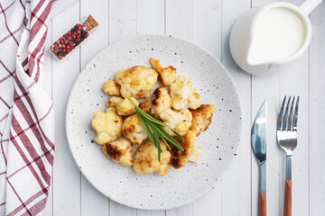 Fried cauliflower florets in batter on a white plate. White wooden background.