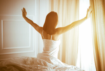 Woman stretching in bed after waking up, back view, entering a day happy and relaxed after good night sleep. Good morning and new day for brunette. Concept of Weekend, holidays