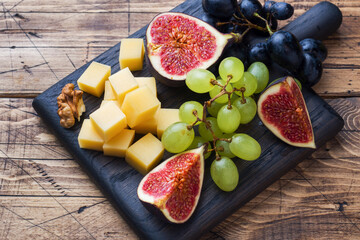 Cheese cubes, fresh fruit figs grapes Honey walnut on wooden chopping Board. Selective focus. Close...