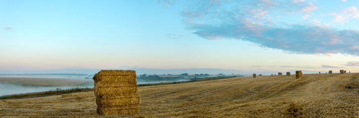 Fototapeta na wymiar Panorama of haystacks in farm field during foggy sunrise