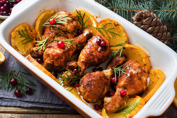 Baked chicken drumstick with oranges and cranberries in a baking sheet on a wooden background. Christmas food Table with decorations.