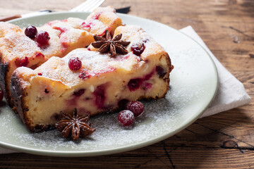 Two pieces of cottage cheese pie casserole with cranberry berries and spices cinnamon and anise on a plate. Wooden background.