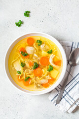 Homemade chicken soup with noodles and vegetables in white bowl, white background, top view.