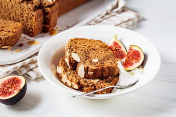 Portion of nut-fruit bread with yogurt and figs. Vegan banana bread, white background.