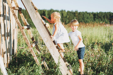 Cute siblings little girl and boy brother sister climbs up the ladder countryside © Galina Zhigalova
