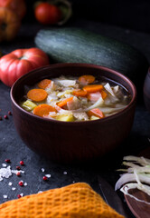 Soup with vegetables and meat in a large clay plate. Soup in a bowl with vegetables on a dark table