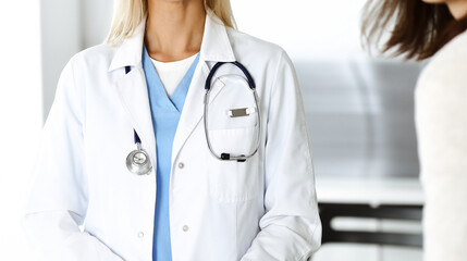 Unknown woman-doctor communicating with female patient. Physician checks medical history record and exam results, close-up. Medicine concept