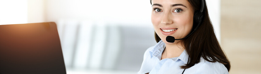 Brunette female customer service representative using headset and consulting clients online. Call center
