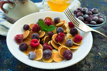 Breakfast of small pancakes with berries and honey and milk. Pancake porridge. Close-up. Fashionable food.