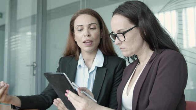 Confident brunette businesswomen carrying out survey with tablet. Red-haired professional young beautiful businesswoman sitting, talking and answering question. Business, company and teamwork concept