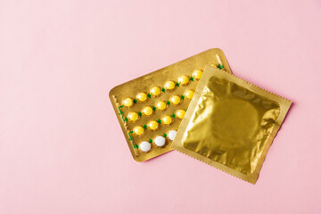 World sexual health or Aids day, condom in wrapper pack and contraceptive pills blister hormonal birth control pills, studio shot isolated on pink background, Safe sex and reproductive health concept