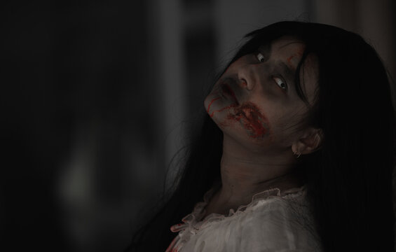 Girl zombie in blood. Closeup face and eyes of Asian Woman ghost with blood. Horror creepy scary fear in a dark house. Hair covering the face, Halloween festival concept
