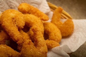 Atlantic shrimps fried in batter on a white paper napkin in a wicker basket. Close up.
