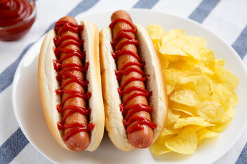 Tasty American Hot Dog with Potato Chips on a white plate, side view. Close-up.