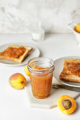Jar of tasty apricot jam and toasted bread on table