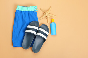 Male swimming trunks with flip-flops and sunscreen on color background