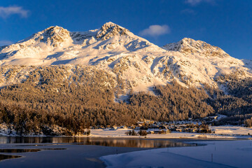 View of beautiful snow mountains behind Lake Silvaplana and its village during a winter sunset