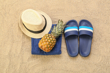 Male flip-flops with towel, hat and pineapple on sand