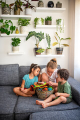 Children learning to knit, sitting on couch in the home. Cozy apartment interior with houseplants.