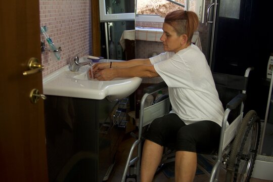 Daily Life Of A Disabled Person In A Wheelchair In The Bathroom Washing Their Hands And Drying Them With A Towel Viewed From The Front