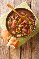 Sausage lentil soup with tomatoes, zucchini, carrots, celery and onions close-up in a plate on the table. vertical top view from above
