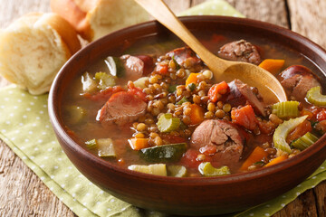 Delicious hot sausage lentil soup with seasonal vegetables close-up in a plate on the table. horizontal
