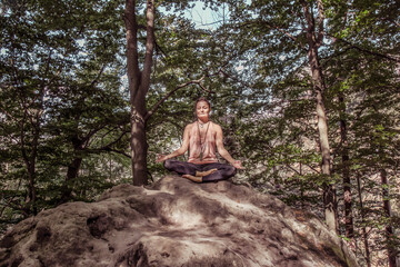 Naklejka na ściany i meble Woman in lotus position meditating on the rock in the forest