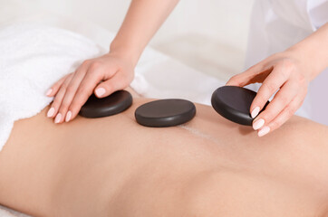 Spa treatments for beauty. Hands lay hot stones on woman back on massage table