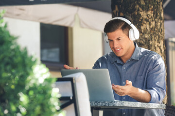 Man with headphones working on laptop in outdoor cafe
