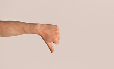 Millennial guy showing thumb down gesture, expressing negativity over light background, copy space