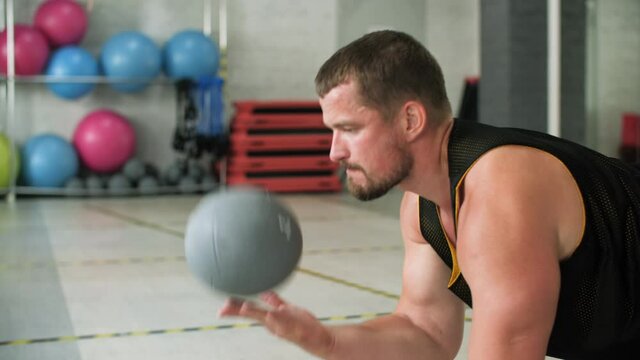 Fitness man throwing med ball while pushing up on floor at cross fit training. Athlete man training push up exercise with ball on gym workout in club