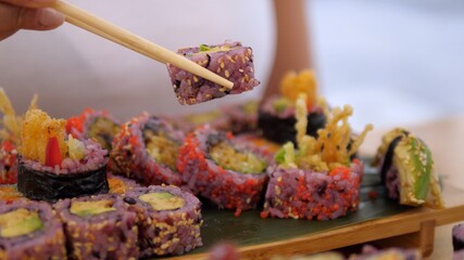 Hand picking one colorful sushi roll with chopsticks. Artisan Asian street food concept