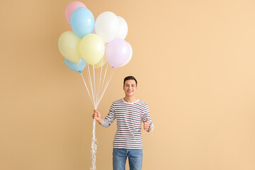Young man with balloons showing thumb-up on color background © Pixel-Shot