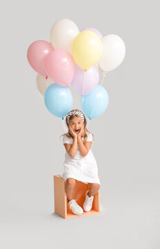 Surprised little girl with balloons on grey background
