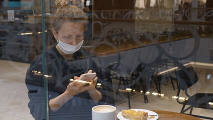 Girl in coffee place using her smartphone at coffee break with coffee and pie during second wave of covid-19 pandemic. 