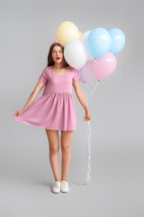 Surprised young woman with balloons on grey background