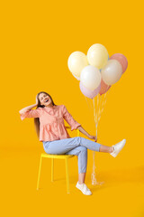 Young woman with balloons sitting on chair against color background