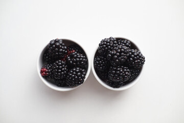 Fresh blackberries in two white cups on white background with space for text