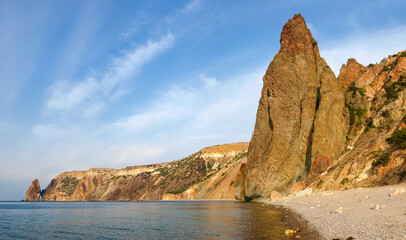 Coastal cliffs above pebble beach on sea against the sky
