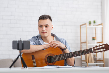 Attractive guy looks at webcam and records video of guitar lesson